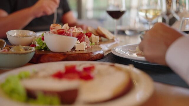 People enjoying shared meal and wine at fancy restaurant table in warm daylight, knife cutting food