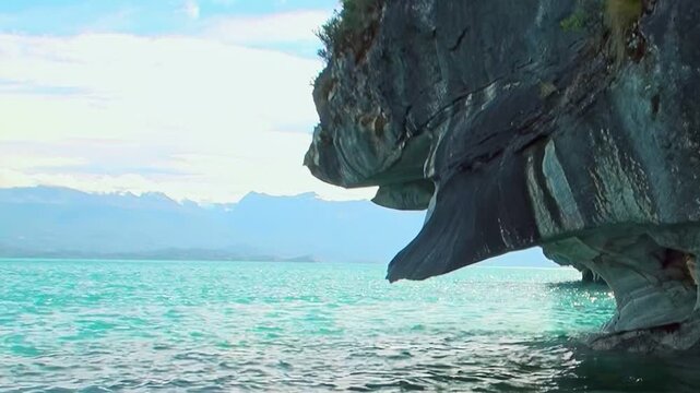 A serene daytime journey unveils the spectacular Marble Caves on General Carrera Lake in Patagonia. Azure waters gently embrace the intricately carved marble grottoes, bathed in bright sunlight.