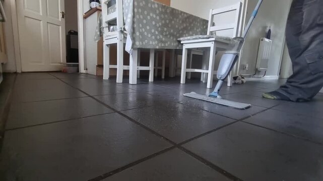 Low angle male wearing socks cleaning tiled kitchen flooring with antibacterial spray mop