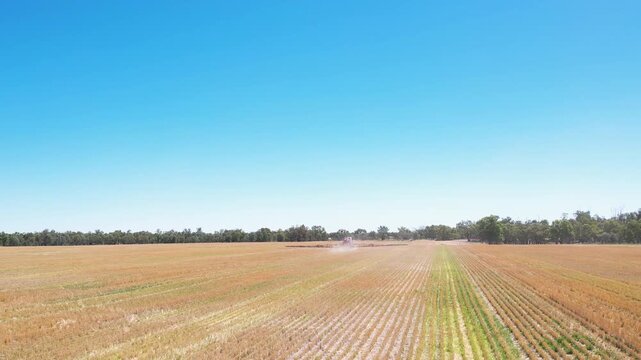 Aerial low alttitude drone view of agricultural sprayer working across harvested field showing crop rows and large scale farming activity in open landscape
