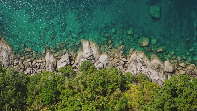 Tropical green jungle meeting clear turquoise water waves and rocky coastline of Phuket, Thailand, beautiful natural environment and tropical landscape wild nature background. Aerial view drone flight