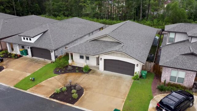 Aerial drone view of suburban houses with landscaped front yards garages and driveways along a residential street showing organized neighborhood layout