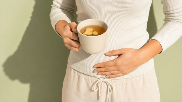 woman holding mug of hot ginger tea while touching stomach. Treatment for digestive pain or nausea. Home remedy for healthy lifestyle and natural stomach relief. Wellness care concept