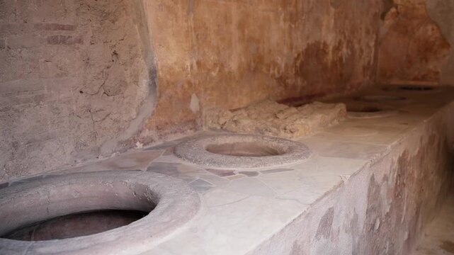 Ancient thermopolium counter in Pompeii with circular dolia openings, weathered plaster walls, and preserved Roman food shop interior details.