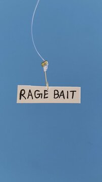 Rage bait word written on a white paper note hooked on a fishing hook like trap or bait. Online media content using rage farming and rage seeding for negative engagement. Ragebait awareness concept.