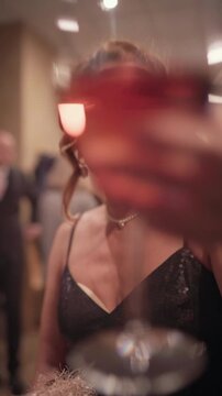 Beautiful retro style woman in black dress with fine makeup smiles and cheers with wine glass at camera. Swing jazz party celebration concept captured in high quality 4K vertical video resolution.