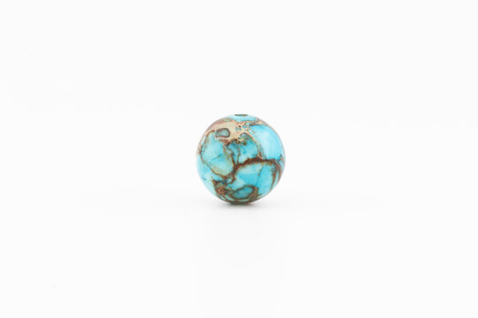A round bead made of variscite sits alone on a plain white background. The bead shows bright colors and distinct lines, highlighting its unique design