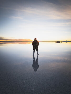 Man watches surreal sunset on reflective salt flats