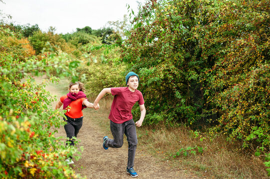 Energetic brother and sister running hand in hand on countryside path
