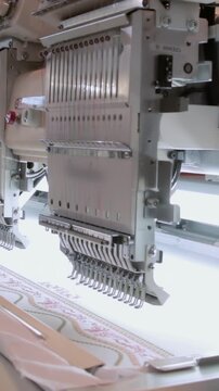A sleek industrial automatic computerized embroidery sewing machine meticulously crafts intricate patterns on white fabric.