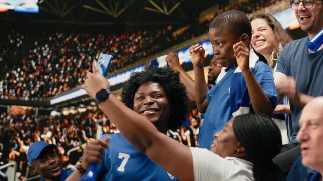 Happy soccer fans taking selfie with child during live match in crowded stadium stands, family outing during first match with cheering supporters group, fun sports and crowd excitement.