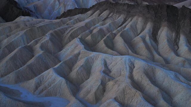 Dramatic Zabriskie Point in Death Valley in badlands formations display intricate ridges Layered sedimentary rock creates wave-like patterns across the barren desert landscape.