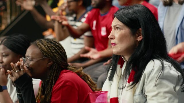 Red team football supporters reacting with anxious gestures in stadium stands during tense live soccer match, scarves and crowd emotion, fans with clenched fists during crucial moment in the match.