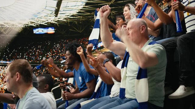 Tense blue team supporters reacting to close call during live soccer match in a crowded stadium, wait for final whistle, multigenerational supporter group shows suspense and anticipation.