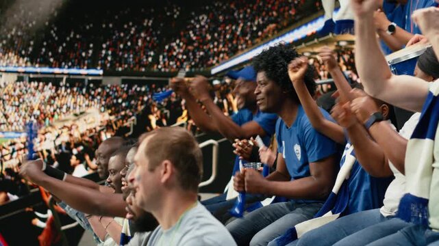 Tense blue team supporters reacting to close call during live soccer match in a crowded stadium, wait for final whistle, multigenerational supporter group shows suspense and anticipation.