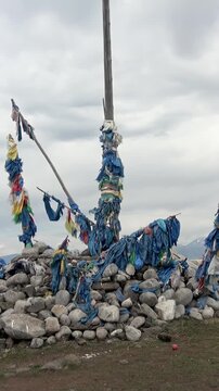 Witness an ancient ovoo shrine, bedecked with vibrant blue and multicolored prayer flags, nestled in the majestic Khuvsgul mountains of Mongolia on a cloudy day. Feel the spirit.