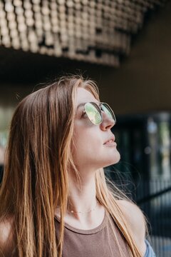 Woman wearing sunglasses looks upward in profile view against architectural background. Visionary mindset, urban perspective, future outlook.