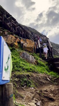 Mom and twin daughters on Robberg hiking trail climb wooden stairs. Vertical