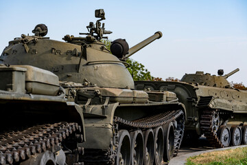 Obraz premium Soviet military tanks and armored vehicles parked outdoor. Closeup view of historic green military armored tanks and infantry fighting vehicles standing in a row on a sunny day under a bright sky