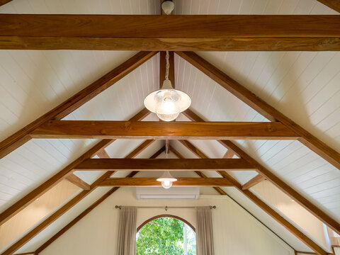 Rustic wooden roof structure with exposed timber beams and warm ceiling lights inside modern loft interior. Cozy architectural design featuring natural wood framework, symmetry, minimal cabin style.