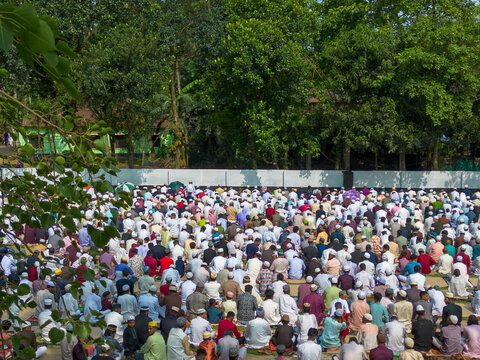 Joypurhat, Bangladesh - 28 May 2026: Aerial view of a large crowd of Muslim men gathered for prayer in an open field surrounded by lush green trees.