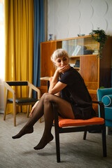 Obraz premium Woman sitting on chair in living room with colorful curtains and furniture in morning light
