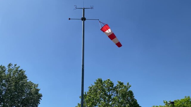 Red and white windsock blowing in the wind against a clear blue sky. Airport wind cone with weather vane indicator showing wind direction and speed. 4K