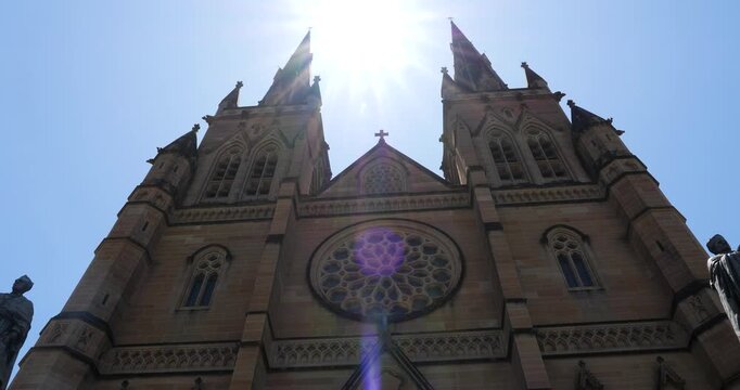St. Mary's Cathedral with its Gothic facade and the sun between the spires, the sun's rays shining off the cross. Sydney, Australia.