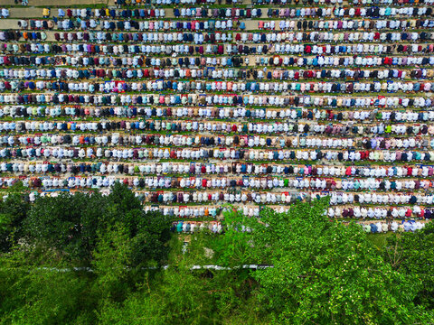 Joypurhat, Bangladesh - 28 May 2026: Aerial view of a large crowd of Muslim men performing congregational prayer in rows on colorful mats next to green trees.