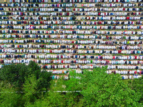 Joypurhat, Bangladesh - 28 May 2026: Aerial view of a large crowd of Muslim men performing Eid prayer in neat rows on colorful mats next to green trees.