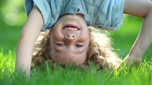 Funny kid do a handstand in a summer park on green grass. Slow motion