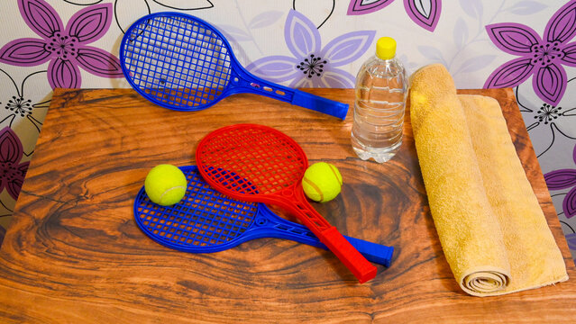 children tennis rackets, balls and water bottle on wooden table