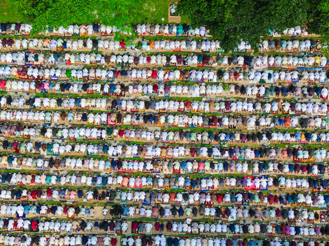 Joypurhat, Bangladesh - 28 May 2026: Aerial view of a large crowd of Muslim worshippers performing Eid prayers in organized rows on colorful mats outdoors.