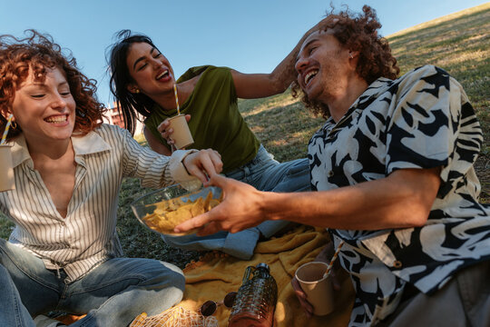 Young friends laughing and sharing snacks during picnic
