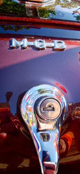 Saint Petersburg, Russia - May 23, 2026: Close-up of MGB car emblem and lock mechanism on a vintage automobile with shiny red paint reflecting surrounding elements
