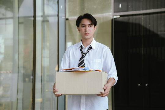 Former employee carrying a box of personal belongings after job termination, symbolizing unemployment, workforce reduction, career transition, and economic uncertainty.
