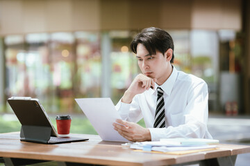 Fototapeta premium Young professional reviewing documents at an outdoor workspace, showing concern about employment, financial matters, career decisions, and business challenges.