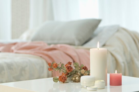 Candles, skin cream and bunch of roses on table with bed in background