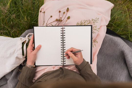 Woman sitting on a meadow writing down something in her notebook, partial view
