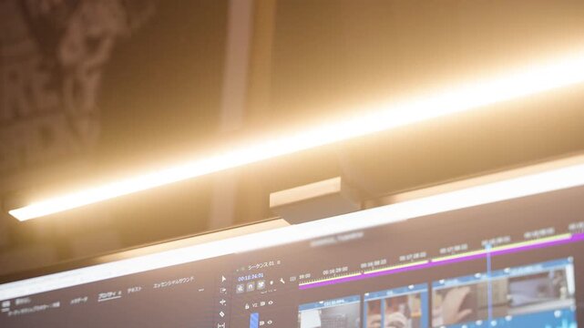 モニターライトに照らされた動画編集ソフトの画面とスタイリッシュなデスク環境/Stylish monitor light illuminating a video editing software screen in a workspace