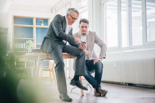 Senior businessman showing cell phone to young businessman