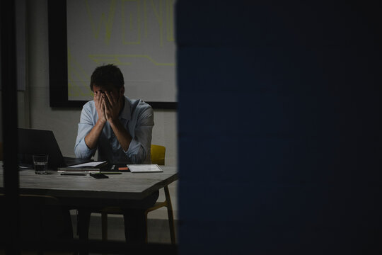Exhausted businessman covering face, sitting in office, working late