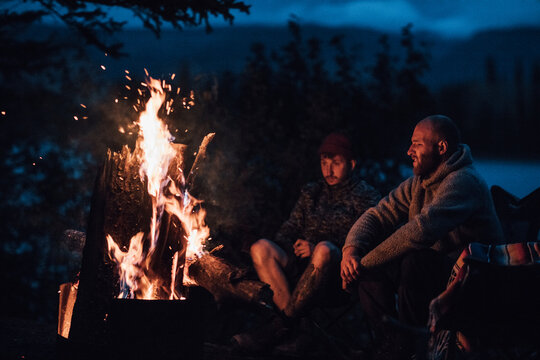 Canada, British Columbia, two men sitting at camp fire at Boya Lake at night