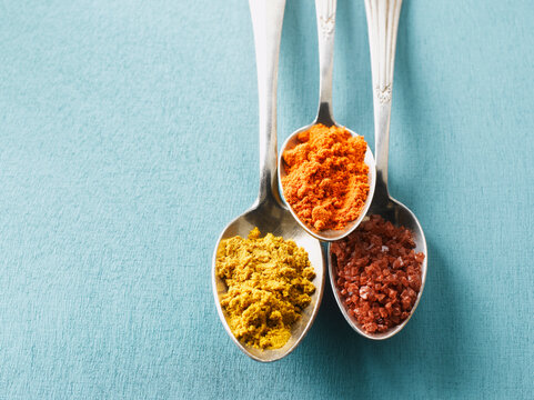 Cayenne pepper, Curry powder and rock salt on spoons, elevated view