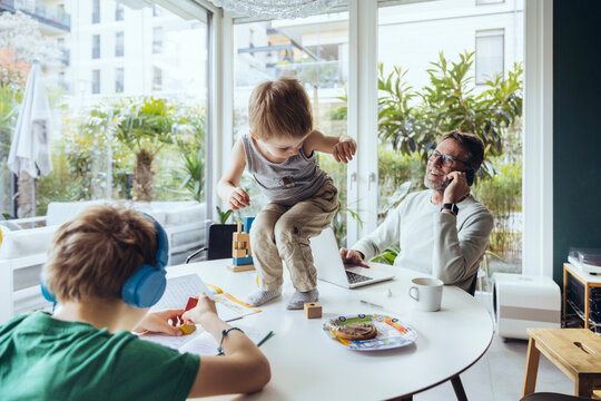Father talking on the phone while sons are playing on the table