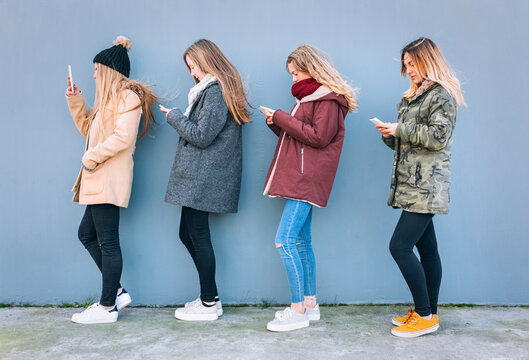 Four young women standing in a row using their cell phones