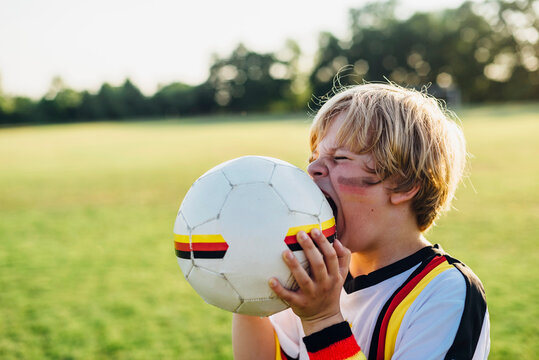 Boy with face paint and German football shirt, biting soccer ball