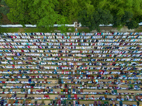 Joypurhat, Bangladesh - 28 May 2026: Aerial view of a large congregation of Muslim men performing prayers in neat rows on colorful mats in an outdoor field bordered by lush green trees.