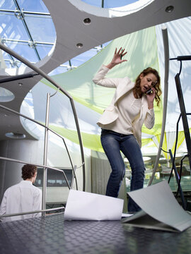 Young businesswoman using mobile phone, papers falling on floor