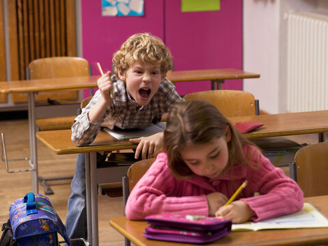 Boy (4-7) shouting behind girl in class room